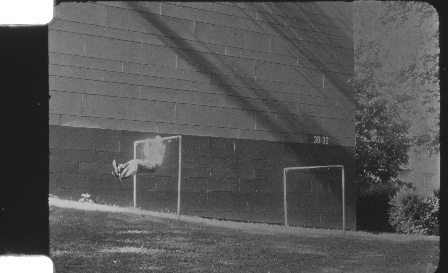 Black-and-white figure suspended against an exterior wall beside a sports field