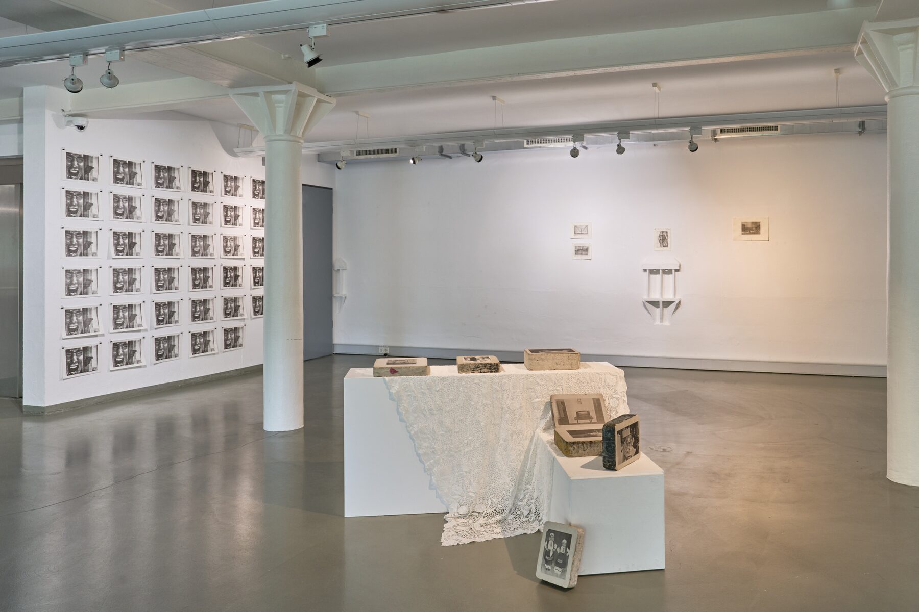 Installation view with photographic prints on lithographic stones, black plinths and lace textiles