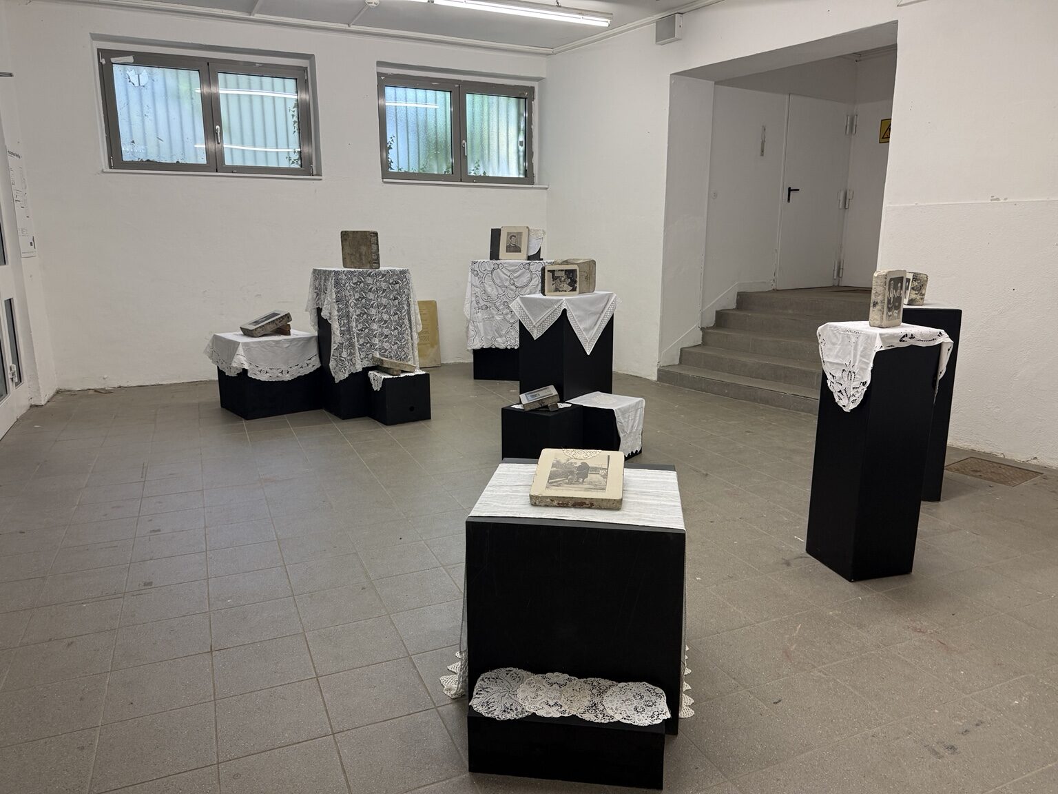 Installation view with lithographic stones, black plinths and lace textiles